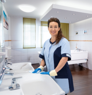 Reinigungskraft säubert Waschbecken im Pflegebad