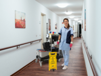 Reinigungskraft mit Reinigungswagen im Flur einer Pflegeeinrichtung