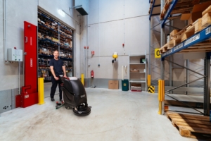 Mitarbeiter des RWS Gebäudeservice reinigt mit einer Bodenreinigungsmaschine die Flächen eines modernen Lagers.