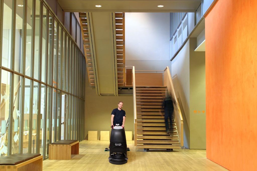 Mitarbeiter von RWS Gebäudeservice reinigt mit einer Bodenmaschine den Flur eines modernen Museumsgebäudes.