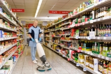 Mitarbeiterin des RWS Gebäudeservice reinigt mit einer Maschine die Böden in einem Supermarktgang.