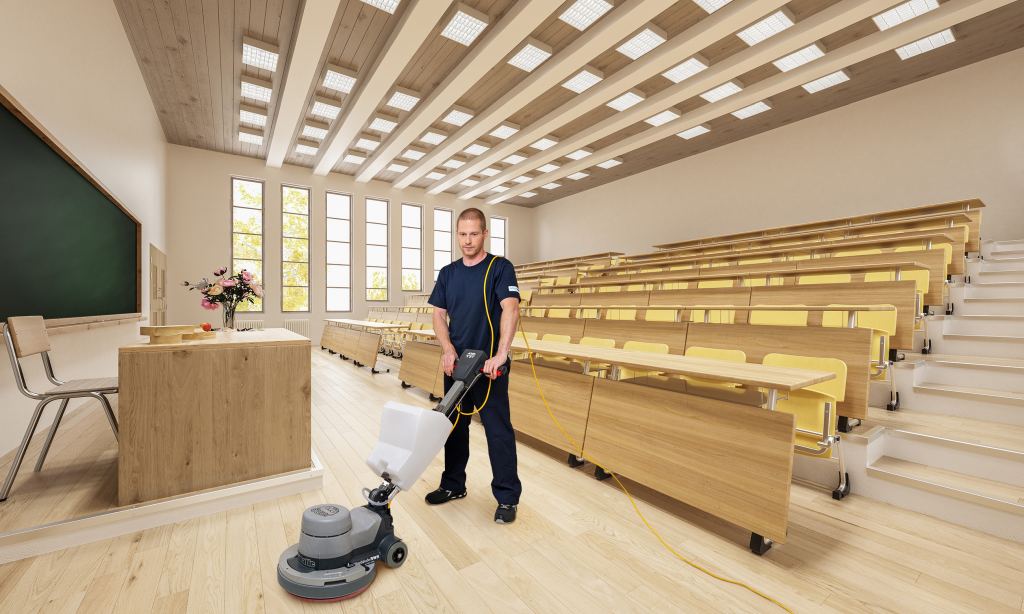 Mitarbeiter von RWS Gebäudeservice fährt mit einer Einscheibemaschine den Hartbodenbelag des Vorlesungssaals in einer Universität im Rahmen der Grundreinigung ab.
