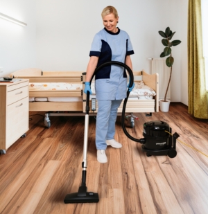 Reinigungskraft saugt den Boden in einem Patientenzimmer