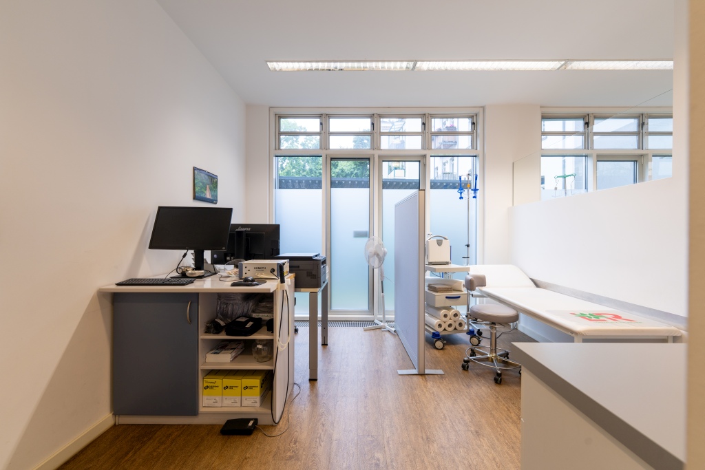 Heller Behandlungsraum in einer Arztpraxis mit Liege, Computer und medizinischer Ausstattung